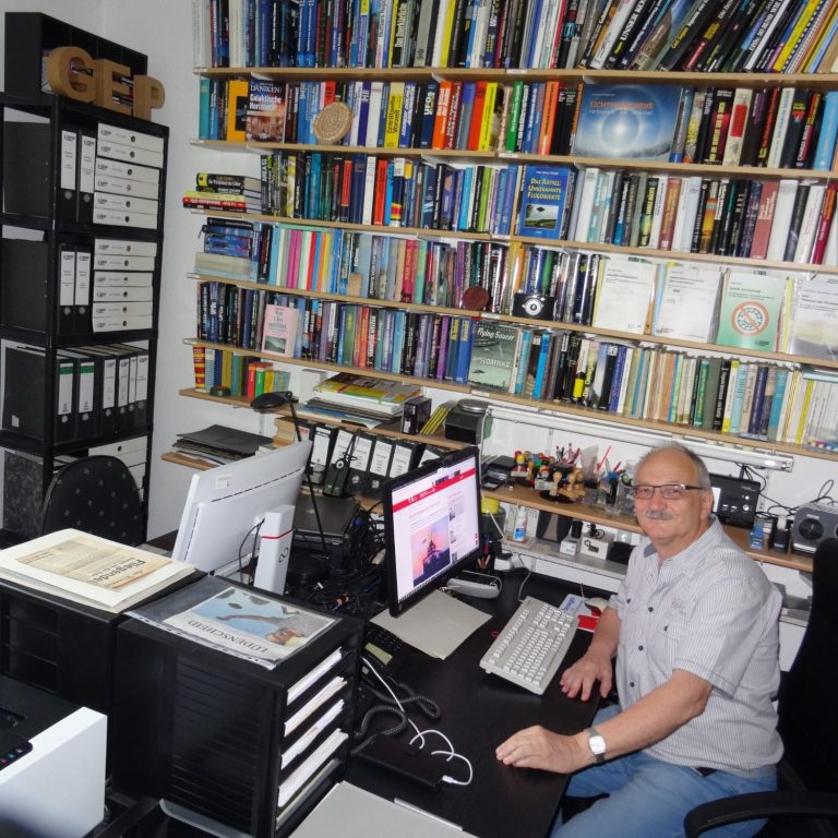 Hans-Werner Peiniger im GEP-Büro in Lüdenscheid Ein älterer Mann sitzt an einem Schreibtisch, umgeben von Bücherregalen und Computerbildschirmen.